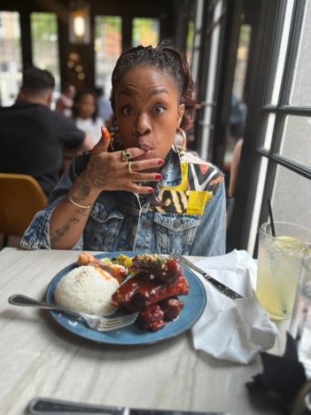 Caira wearing a jean jacket, licking lips in New Orleans with plate of BBQ