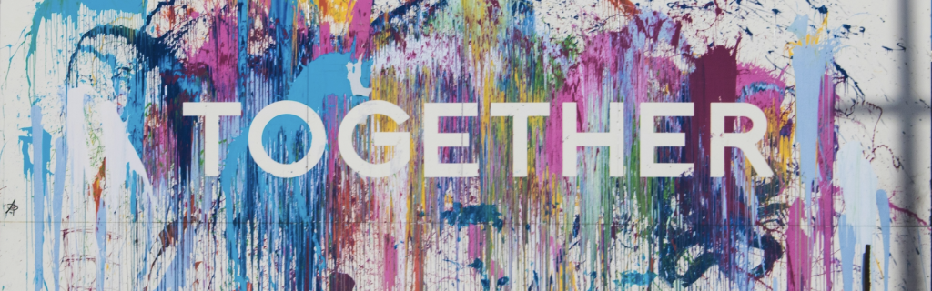 The word Together with multicolored paint splattered around it on a white wall