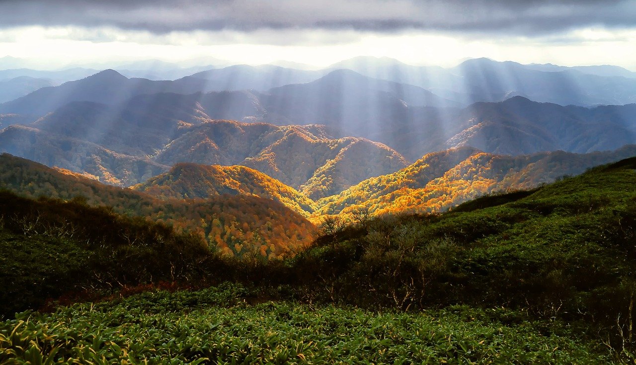 Sun peaking through the clouds over a mountain range with autumn leaves