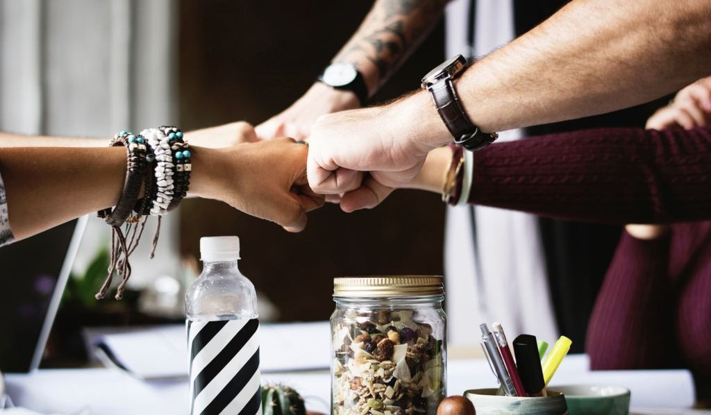 five people's fists coming together for a fist bump with some bottles in the foreground