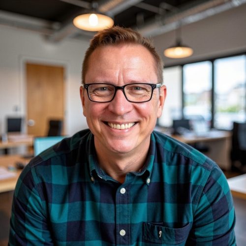 Matt is a white man with short brown hair, glasses, and no facial hair. He's wearing a collared green and blue checked shirt and smiling in this portrait with a blurred background